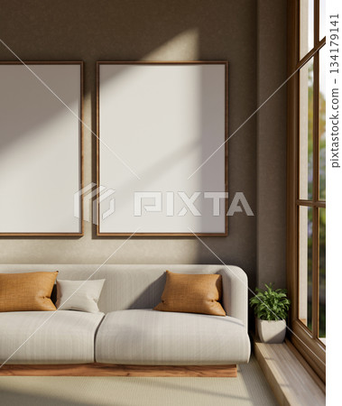 White frames hanging over fabric sofa with cushion and houseplant aside window in modern living room 134179141