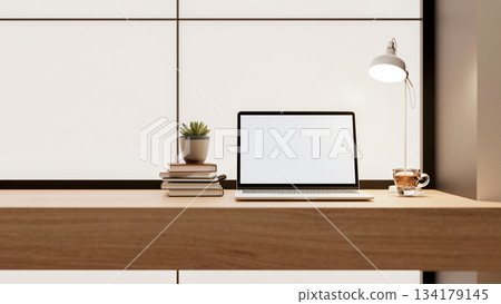 Blank screen laptop with books and coffee cup aside lamp on wooden table in a glass tiles wall room. 134179145