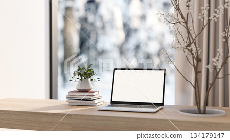 White screen computer and books with dried branch through wooden table and snow outside glass wall. 134179147