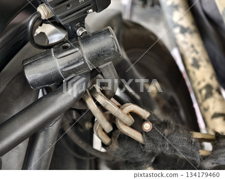 Close-up of a motorcycle security chain and lock attached to the frame. Shows details of metal links, padlock, and protective sleeve, ideal for illustrating security, protection, and anti-theft Close-up of a motorcycle security chain and lock attached to the frame. Shows details of metal links, padlock, and protective sleeve, ideal for illustrating security, protection, and anti-theft 134179460