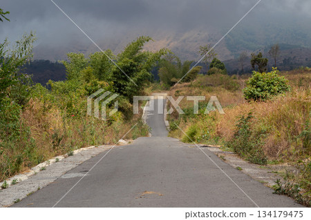 Empty asphalt road leading steeply uphill into misty mountains and thick dark clouds Empty asphalt road leading steeply uphill into misty mountains and thick dark clouds 134179475
