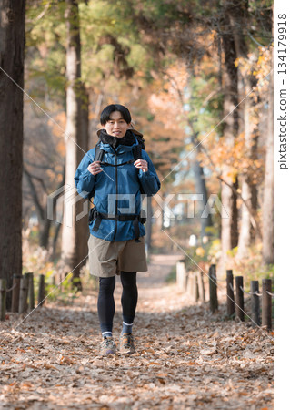 A young man climbing a mountain covered in autumn leaves, smiling and looking at the camera 134179918