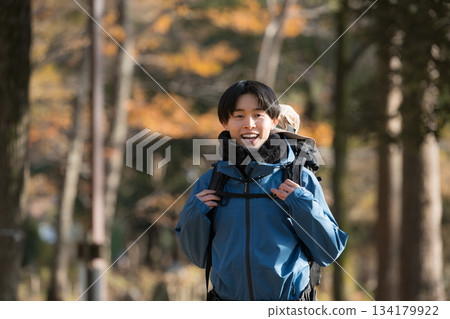 A young man climbing a mountain covered in autumn leaves, looking at the camera and enjoying the scenery A young man climbing a mountain covered in autumn leaves, looking at the camera and enjoying the scenery 134179922