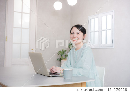 Smiling cute woman using a computer at home or in a cafe, looking at the camera 134179928
