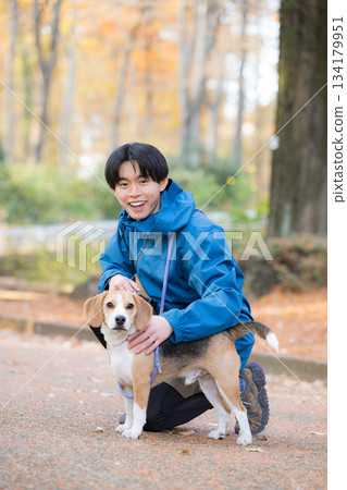 一位微笑的男子在秋日的公園裡遛狗，享受著與愛犬相處的時光，並看向鏡頭。 134179951