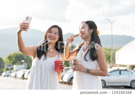 Pretty asian woman holding drink cup and taking photo with a friend while standing in local market 134180166