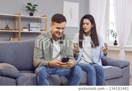 Young couple sitting on sofa at home using mobile phone ignoring each other in living room. 134181481