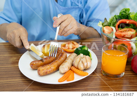 Asian senio woman patient eating breakfast with vegetable healthy food while sitting and hungry on bed in hospital. Asian senio woman patient eating breakfast with vegetable healthy food while sitting and hungry on bed in hospital. 134181687