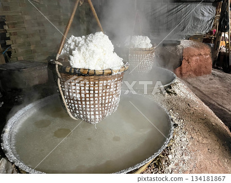 Traditional salt boiling process with baskets of crystallized salt hanging over steaming brine, showcasing rustic craftsmanship and local production methods 134181867