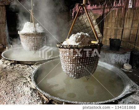 Traditional salt boiling process with baskets of crystallized salt hanging over steaming brine, showcasing rustic craftsmanship and local production methods 134181868