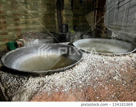 Traditional salt boiling process with baskets of crystallized salt hanging over steaming brine, showcasing rustic craftsmanship and local production methods Traditional salt boiling process with baskets of crystallized salt hanging over steaming brine, showcasing rustic craftsmanship and local production methods 134181869