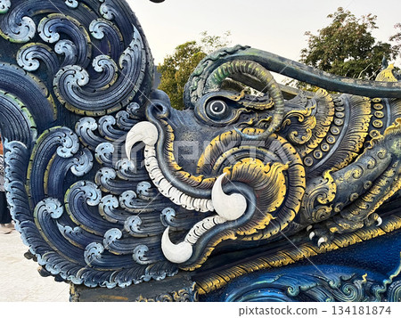 A detailed sculpture of a mythical guardian figure in vibrant blue and gold, showcasing ornate Thai craftsmanship with rich textures and cultural artistry 134181874