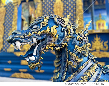 A detailed sculpture of a mythical guardian figure in vibrant blue and gold, showcasing ornate Thai craftsmanship with rich textures and cultural artistry A detailed sculpture of a mythical guardian figure in vibrant blue and gold, showcasing ornate Thai craftsmanship with rich textures and cultural artistry 134181879