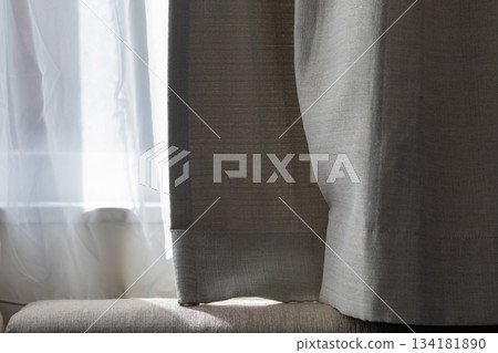 Soft sunlight filtering through white sheer curtains onto the sofa Soft sunlight filtering through white sheer curtains onto the sofa 134181890