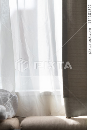 Soft sunlight filtering through white sheer curtains onto the sofa Soft sunlight filtering through white sheer curtains onto the sofa 134181892