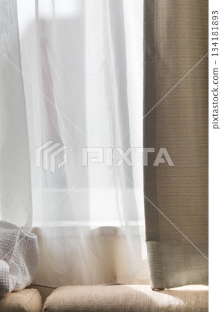 Soft sunlight filtering through white sheer curtains onto the sofa 134181893