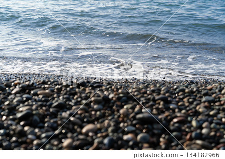 Indulge in a tranquil day at a luxurious spa retreat. The setting features smooth pebbles lining the shore and gentle waves lapping against the coast, creating a peaceful environment. 134182966