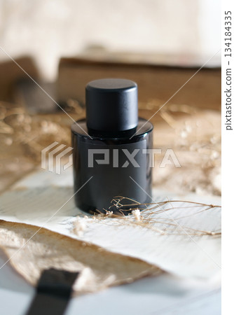 Elegant black bottle sits on a background with aesthetic ornaments with delicate color tones. A perfect vintage charm to a rustic still life, perfect for fashion, fragrance, or lifestyle projects Elegant black bottle sits on a background with aesthetic ornaments with delicate color tones. A perfect vintage charm to a rustic still life, perfect for fashion, fragrance, or lifestyle projects 134184335
