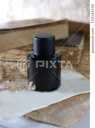 Elegant black bottle sits on a background with aesthetic ornaments with delicate color tones. A perfect vintage charm to a rustic still life, perfect for fashion, fragrance, or lifestyle projects Elegant black bottle sits on a background with aesthetic ornaments with delicate color tones. A perfect vintage charm to a rustic still life, perfect for fashion, fragrance, or lifestyle projects 134184336