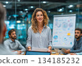 A confident businesswoman leads a meeting, standing with notes in hand, presenting ideas to her team in a modern office with a creative whiteboard behind her. 134185232