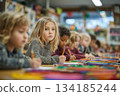 Children sit together in a colorful classroom, focused on drawing and writing. One child looks up thoughtfully, capturing a moment of learning and creativity. 134185244