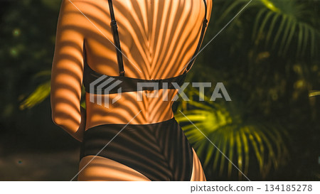 Close up rear view woman back wearing black bikini top sun palm leaf shadow skin tan summer vacation tropical nature artistic beauty wellness Close up rear view woman back wearing black bikini top sun palm leaf shadow skin tan summer vacation tropical nature artistic beauty wellness 134185278