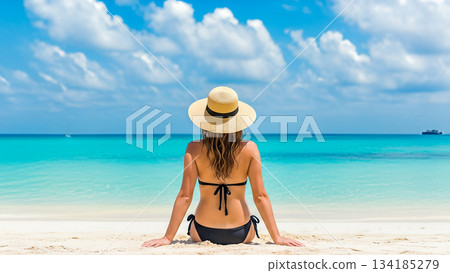 Rear view woman sitting white sand beach wearing straw hat black bikini looking turquoise ocean water summer vacation travel holiday tropical relax 134185279