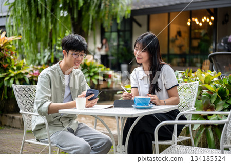 Glasses asian man showing phone to woman student holding tablet's pen at table in the cafe's garden 134185524