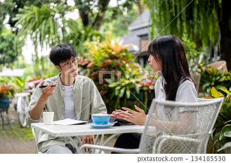 Glasses asian man holding pen and woman student talking as doing assignment at table in cafe's garden 134185530