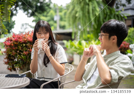 Pretty asian woman drinking coffee and talking with glasses man while sitting at table in cafe garden 134185539