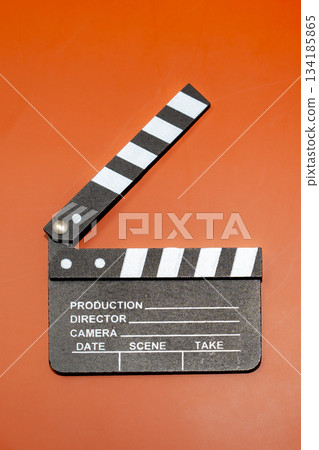 A film clapperboard on an orange background, used in the movie industry. The slate is opened to indicate the start of a film. A film clapperboard on an orange background, used in the movie industry. The slate is opened to indicate the start of a film. 134185865