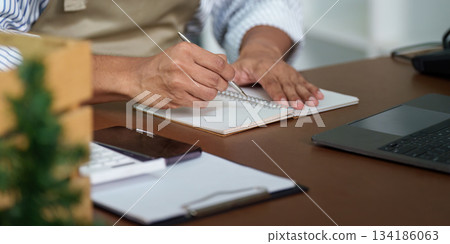 Productivity and Planning. A focused individual writing notes in a notebook at a modern workspace. 134186063