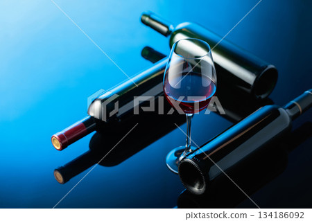 Glass and bottles of red wine on a black reflective background. Glass and bottles of red wine on a black reflective background. 134186092