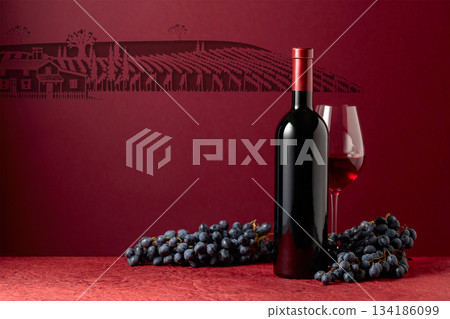 Bottle and glass of red wine with blue grapes on a red background. Bottle and glass of red wine with blue grapes on a red background. 134186099