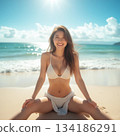 A woman in a swimsuit sitting with her legs apart on the beach 134186291
