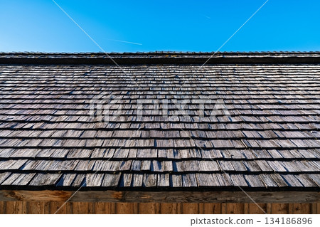 Weathered Wooden Shingle Roof Texture Against a Vivid Blue Sky on a Sunny Day. 134186896