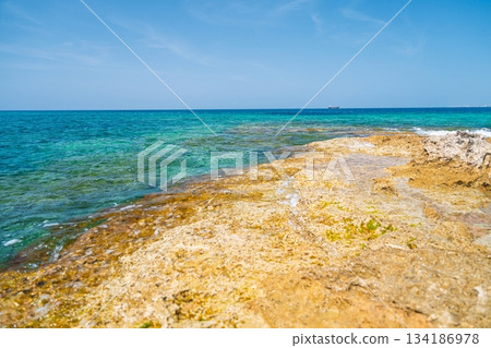 Tranquil Turquoise Waters Meet Golden Rocky Shoreline Under a Clear Blue Sky, Serenity Tranquil Turquoise Waters Meet Golden Rocky Shoreline Under a Clear Blue Sky, Serenity 134186978