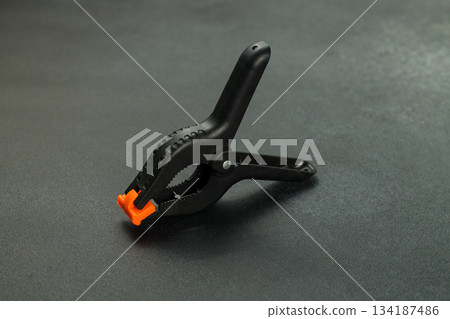 Black Spring Clamp Tool with Orange Tips on Dark Background Black Spring Clamp Tool with Orange Tips on Dark Background 134187486
