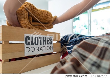 Clothes Donation. Hand placing knitted sweater into donation box. Clothes Donation. Hand placing knitted sweater into donation box. 134187533
