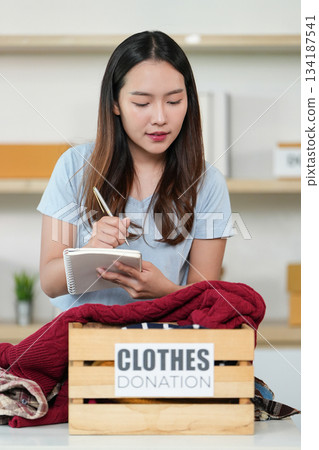 Clothes Donation. Young woman taking notes while donating clothes. 134187541