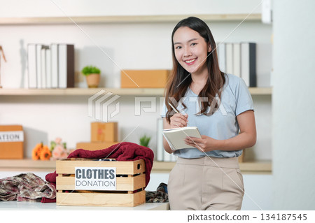 Clothes Donation. Smiling woman documenting clothing donations. 134187545
