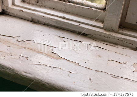 Window sill of an old house reveals significant damage with peeling paint and discoloration. The scene reflects years of neglect and the need for repairs in this aging space Window sill of an old house reveals significant damage with peeling paint and discoloration. The scene reflects years of neglect and the need for repairs in this aging space 134187575