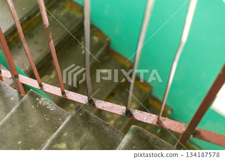 Stairs inside an old house display peeling paint and worn surfaces, surrounded by a vivid green wall. The atmosphere reflects years of wear and tear, emphasizing its condition 134187578