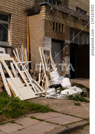 Discarded wooden doors and trash bags clutter the sidewalk outside an old building, creating an eyesore in an urban setting. The sunlight highlights the scene's neglect Discarded wooden doors and trash bags clutter the sidewalk outside an old building, creating an eyesore in an urban setting. The sunlight highlights the scene's neglect 134187605