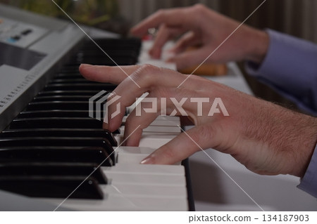 A young white man plays an electronic synthesizer indoors, immersed in his creative hobby. Focused on shaping tones and melodies, he explores musical expression and artistry in a calm home setting. A young white man plays an electronic synthesizer indoors, immersed in his creative hobby. Focused on shaping tones and melodies, he explores musical expression and artistry in a calm home setting. 134187903