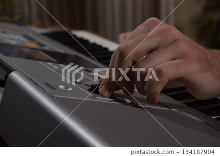 A young white man plays an electronic synthesizer indoors, immersed in his creative hobby. Focused on shaping tones and melodies, he explores musical expression and artistry in a calm home setting. A young white man plays an electronic synthesizer indoors, immersed in his creative hobby. Focused on shaping tones and melodies, he explores musical expression and artistry in a calm home setting. 134187904