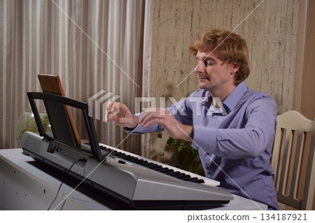 A young white man plays an electronic synthesizer indoors, immersed in his creative hobby. Focused on shaping tones and melodies, he explores musical expression and artistry in a calm home setting. A young white man plays an electronic synthesizer indoors, immersed in his creative hobby. Focused on shaping tones and melodies, he explores musical expression and artistry in a calm home setting. 134187921