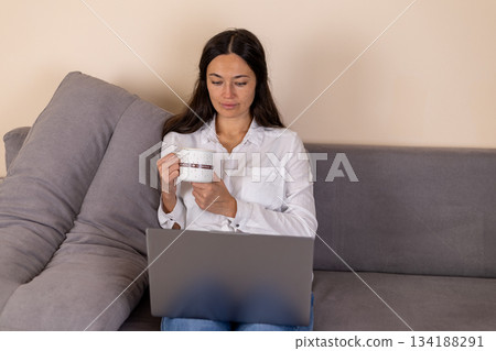 Woman enjoying coffee while working on a laptop at home or in cafe Woman enjoying coffee while working on a laptop at home or in cafe 134188291