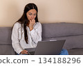 Casual young woman works on a laptop at home, sitting on the sofa 134188296