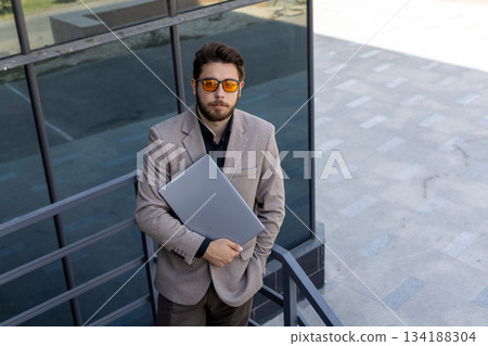 Stylish businessman works on laptop while standing outdoors, full length Stylish businessman works on laptop while standing outdoors, full length 134188304